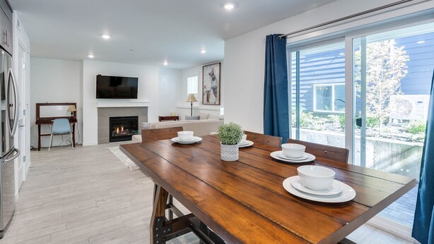A modern dining area with a wooden table set for four, a fireplace, a TV, and a view of the outdoors.