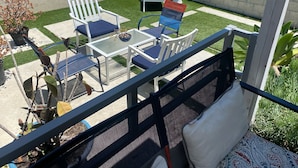 An outdoor patio with a table and chairs, a small garden area, and a view of the street.