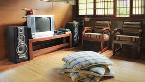 A traditional Japanese room with tatami flooring, a television, speakers, and two wooden chairs. - VILLA ADE - 0224 KOTA BUNGA PUNCAK (Cipanas)