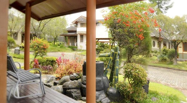 Un espacio al aire libre techado con piso de madera, una jardinera de piedra y diversas plantas y arbustos.