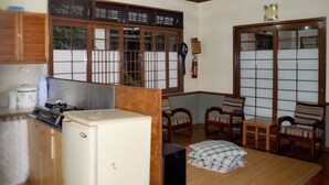 A compact living space with a kitchenette, a dining area with wooden chairs, and a sliding glass door leading to a balcony. - VILLA ADE - 0224 KOTA BUNGA PUNCAK (Cipanas)