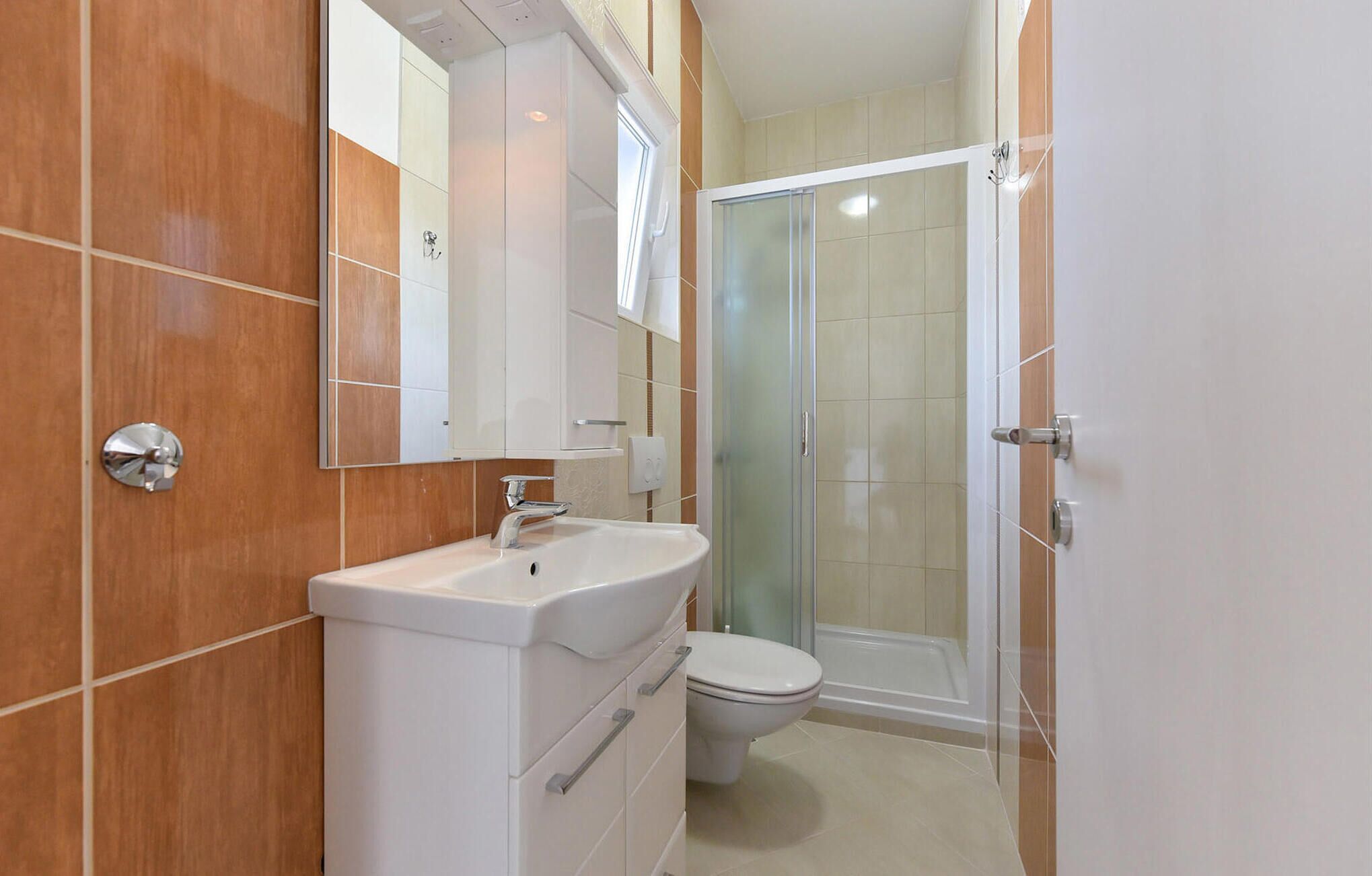 Un bany amb un rentamans, un mirall i un vàter, i una cabina de dutxa de vidre.