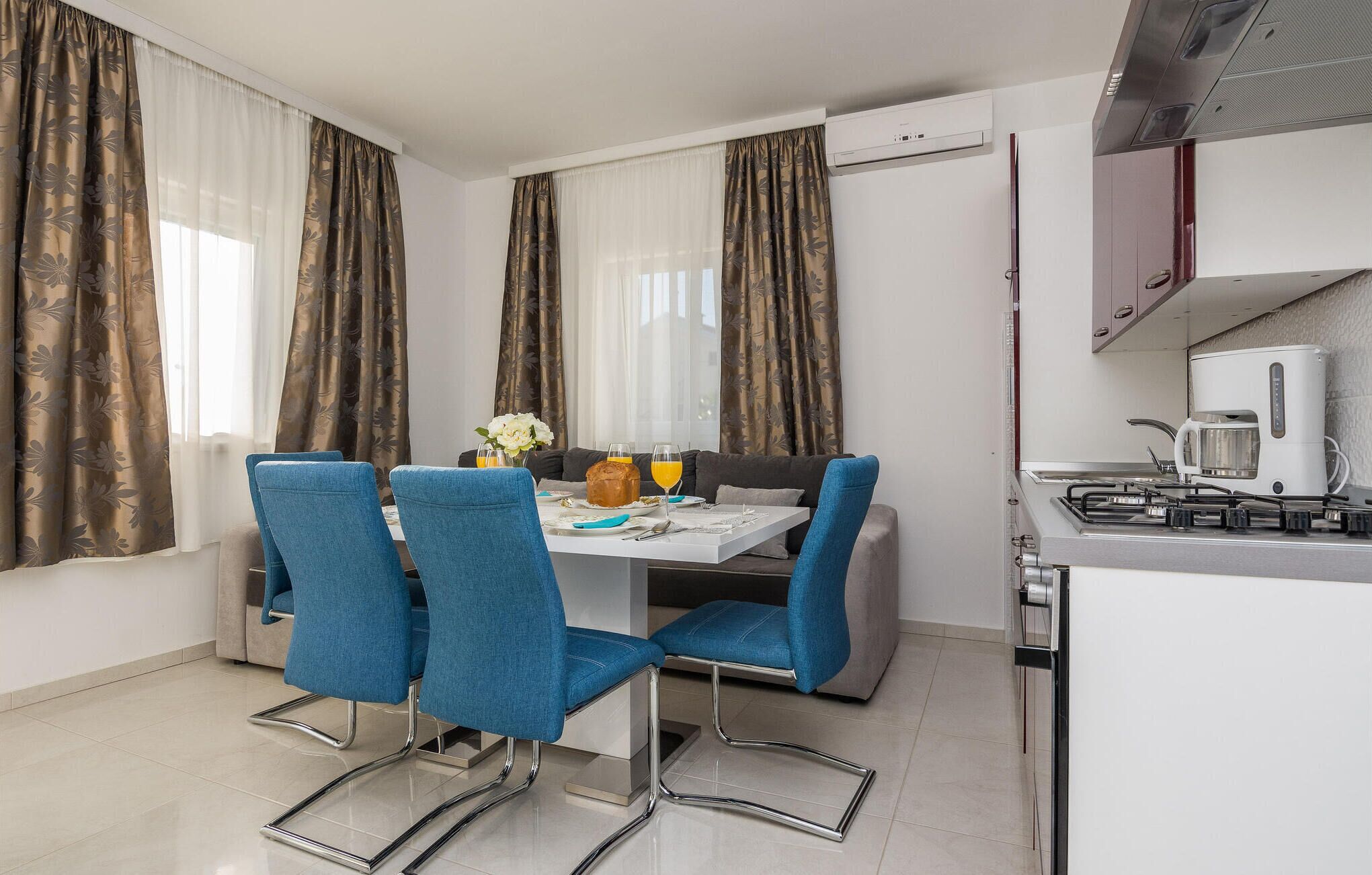 A compact kitchen with a gas stove, a coffee maker, and a small dining area with blue chairs and a table.