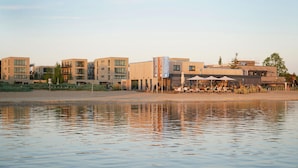 Ein Hotel direkt am Wasser, mit moderner Architektur, Außenbereich zum Sitzen und Blick auf den Strand.