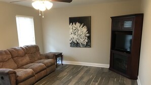 A living room with a brown leather sofa, a small side table, a fireplace, and a large wall-mounted TV. - House near Lee University (Cleveland)