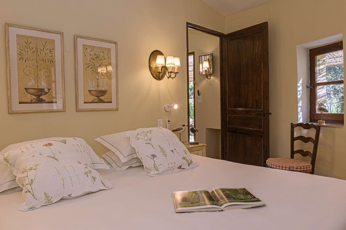 A bedroom with a bed, pillows, a book, a mirror, and wall-mounted lights.