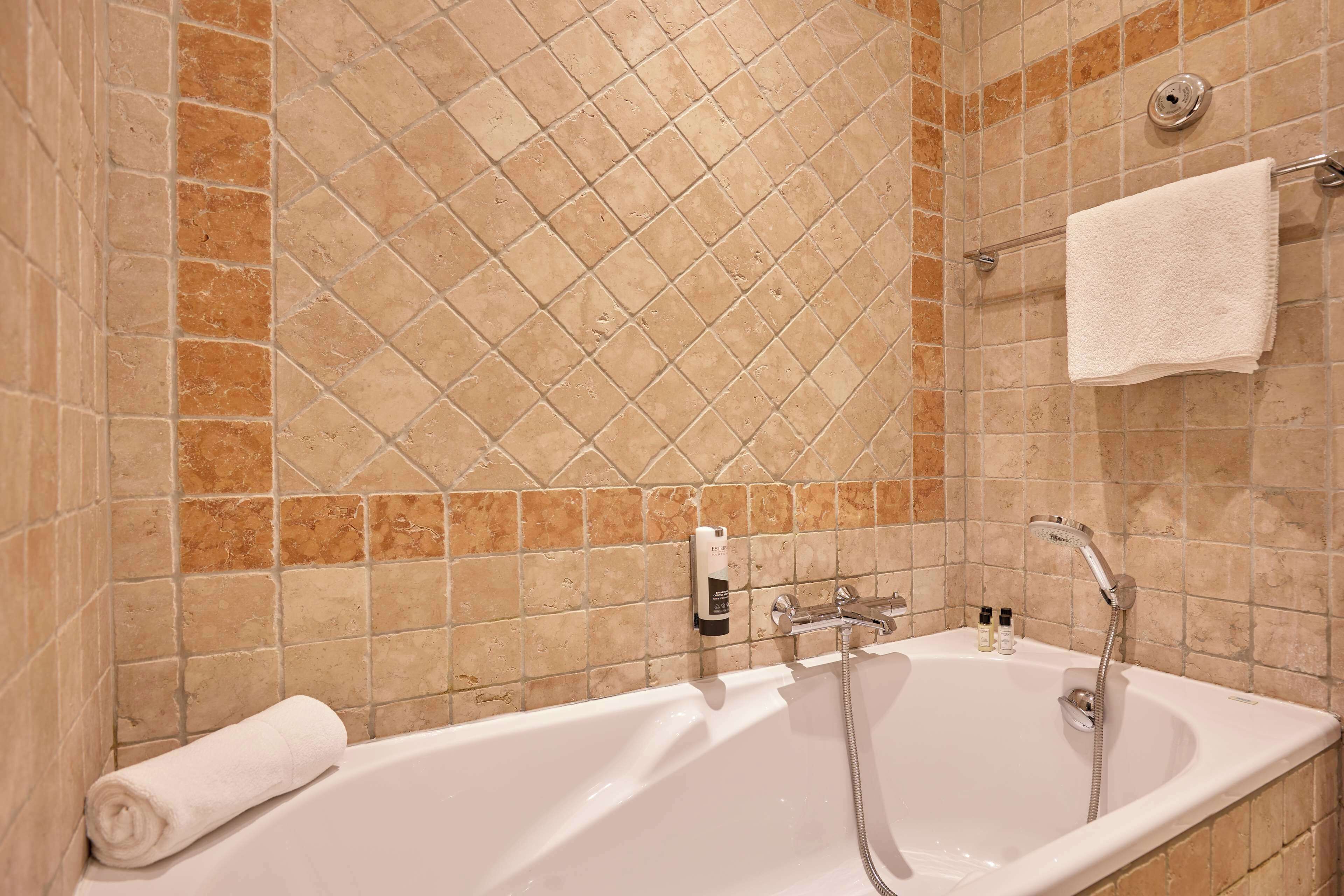 A bathroom with a bathtub, a towel rack, and a soap dispenser.