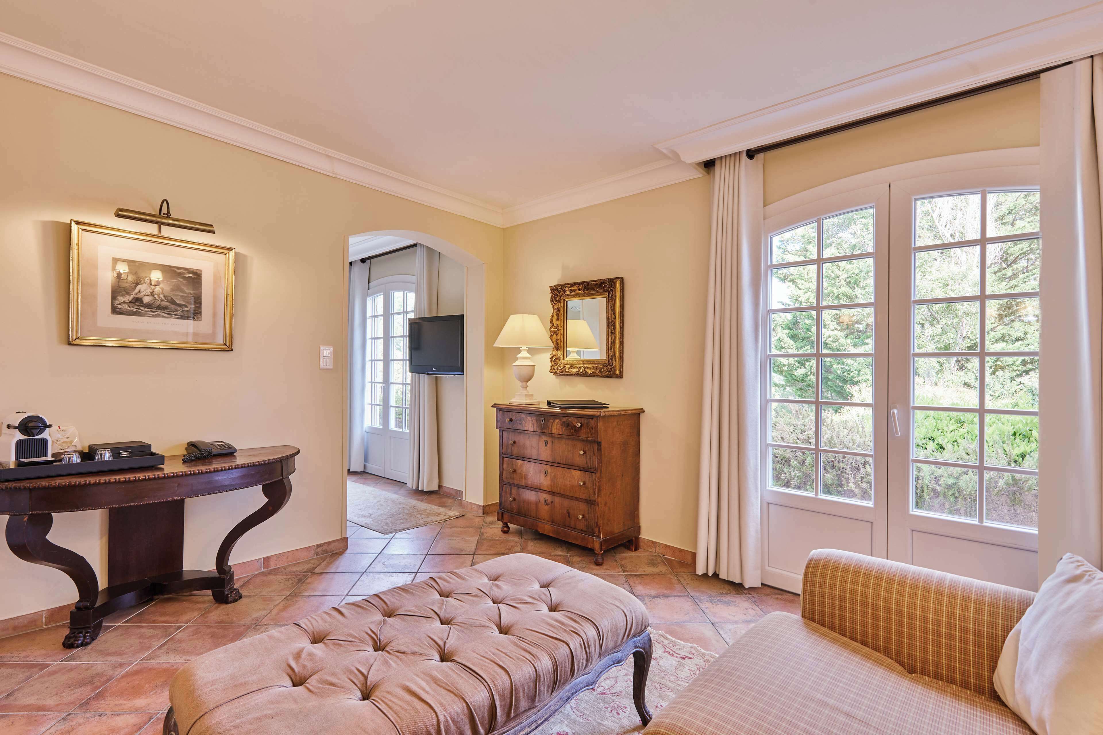 Quarto com uma janela ampla, escrivaninha de madeira, um banco estofado e um sofá.