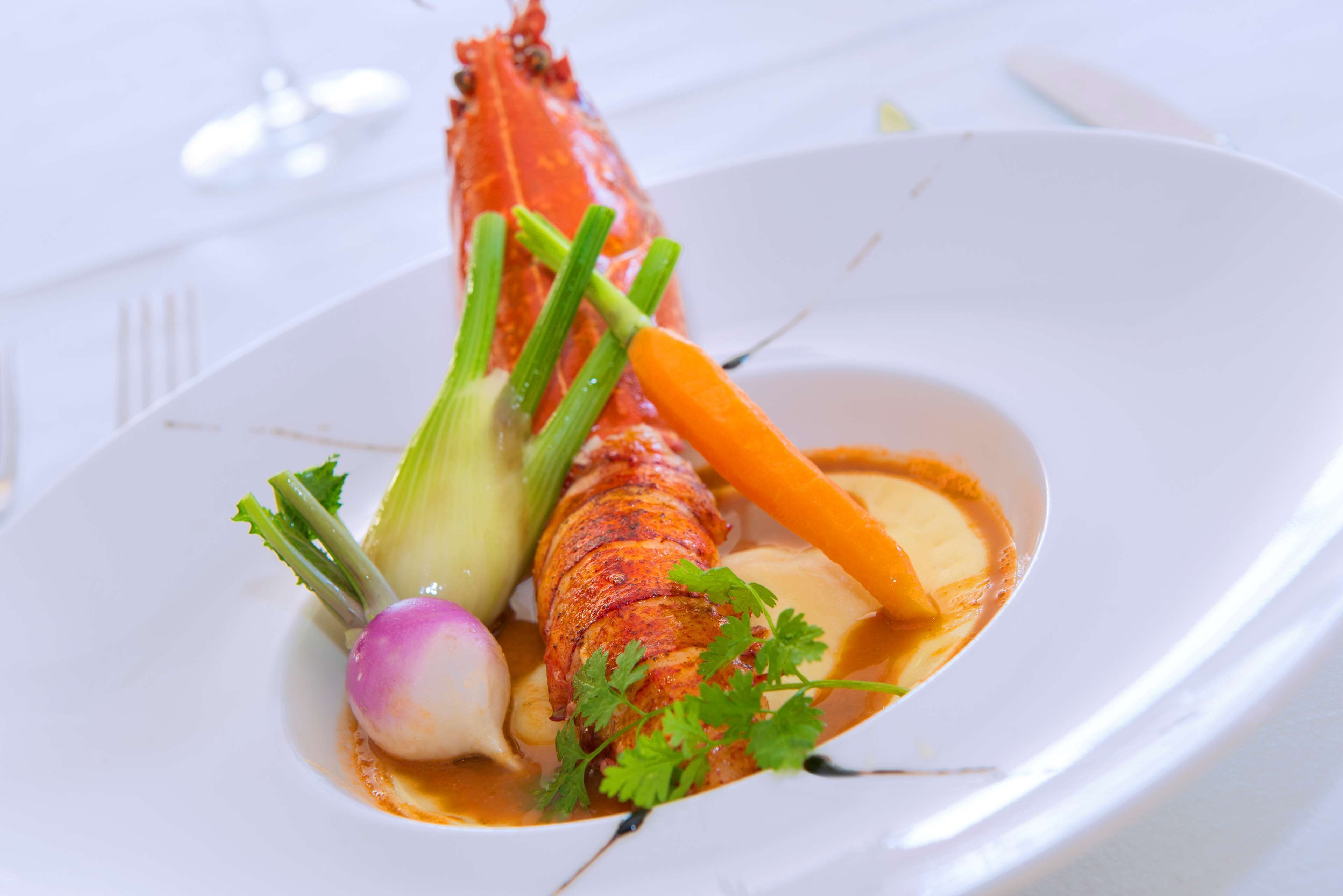 A lobster dish with vegetables and sauce on a white plate.