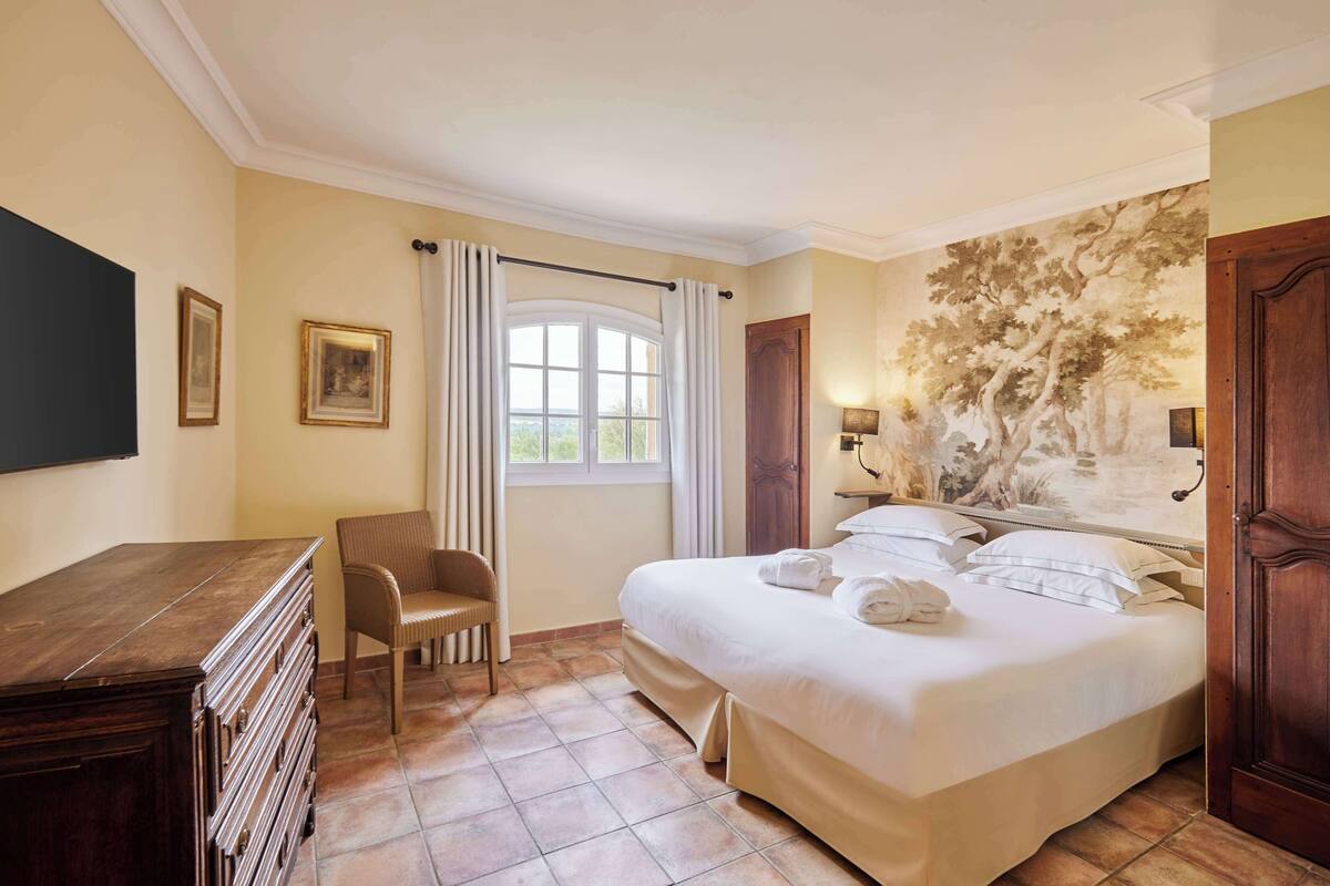 A hotel room with a large bed, a wooden dresser, a chair, and a window with curtains.
