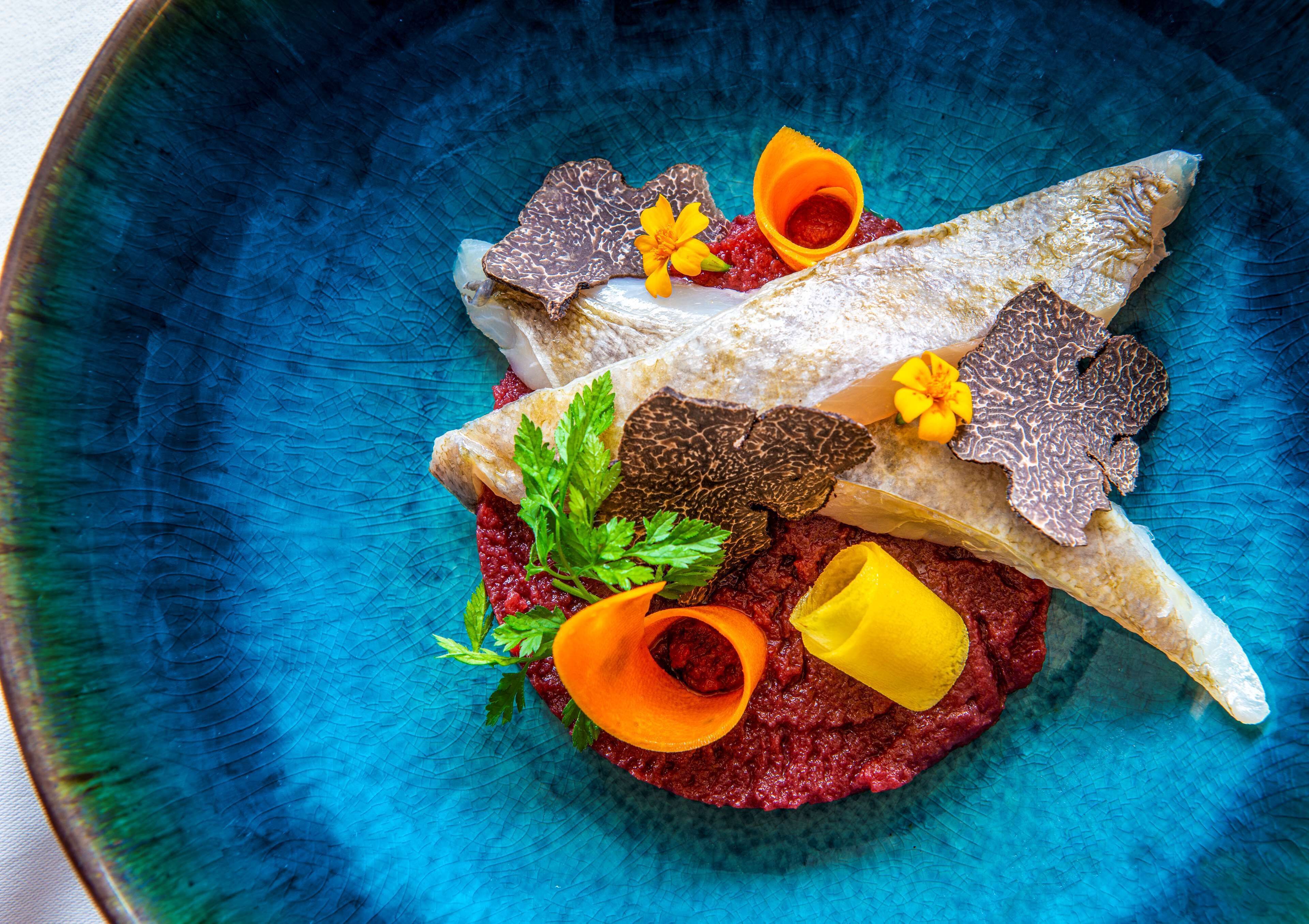 Une assiette bleue contenant un filet de poisson, une sauce rouge et des éléments décoratifs.