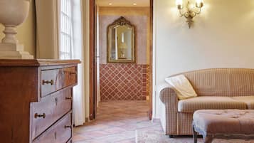 A room with a wooden dresser, a sofa, a patterned rug, a mirror, and a wall-mounted light fixture.