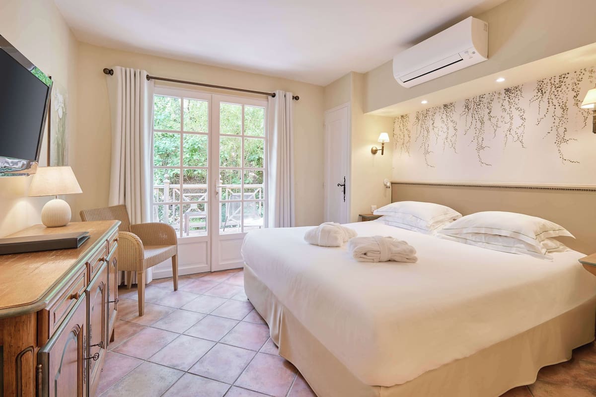 A hotel room with a bed, a desk with a lamp, a chair, a TV, and a window with curtains.