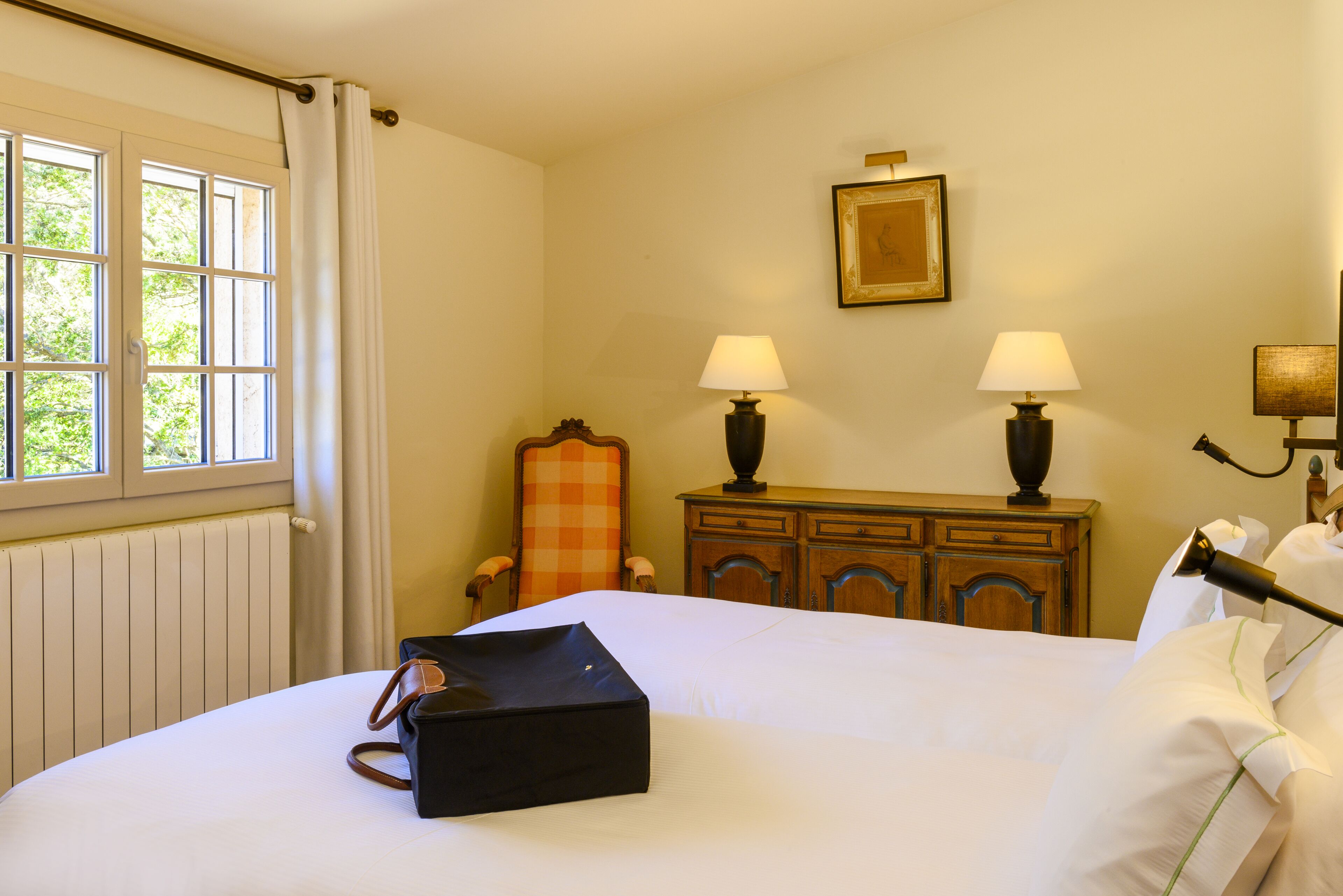 Habitación de hotel con cama, una silla, cómoda, dos lámparas y un cuadro en la pared.