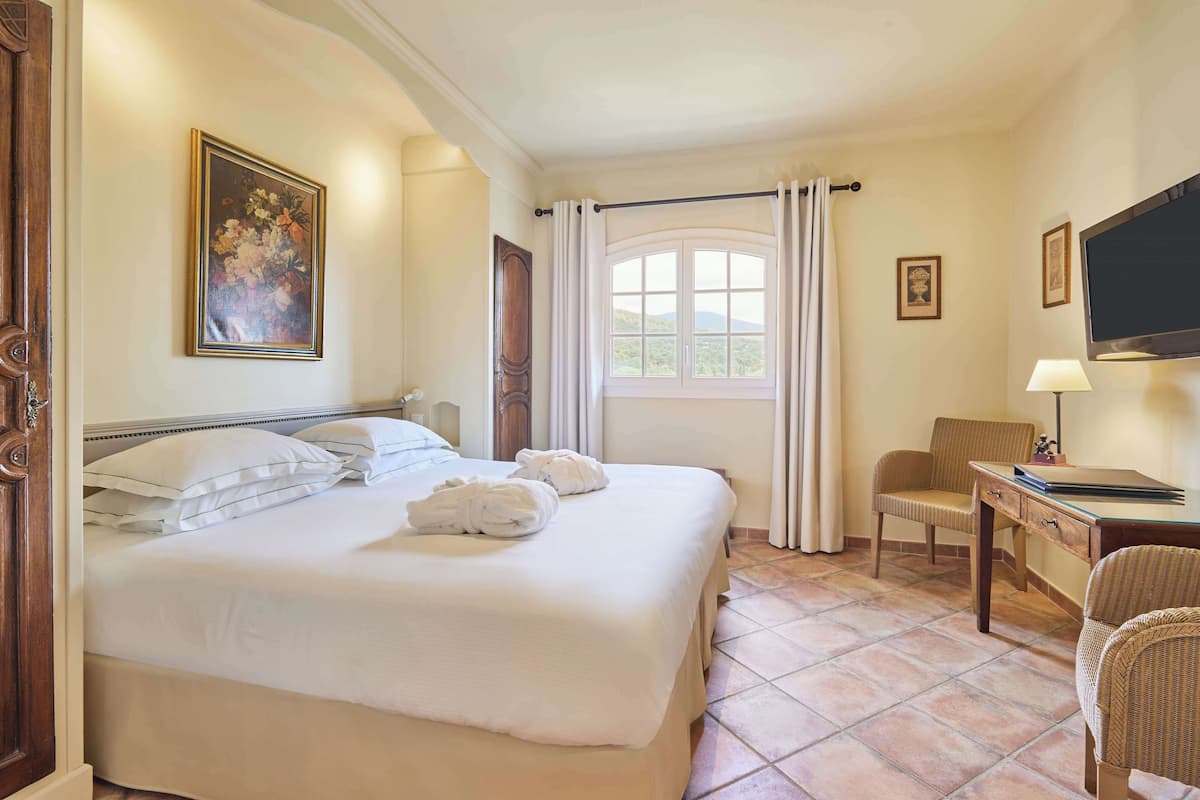 A hotel room with a large bed, a desk with a chair, a television, and a window with curtains.