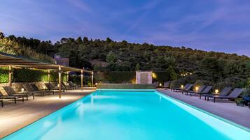 Une piscine dotée de chaises longues et d’une pergola, entourée de verdure et de collines.