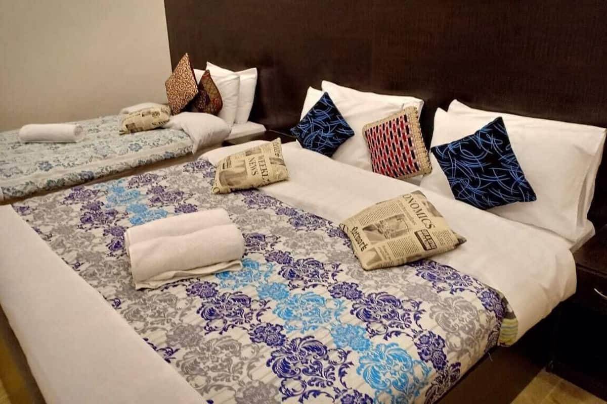 A hotel room with two beds, each with patterned bedding and multiple pillows.