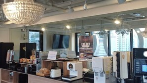 A modern coffee shop with a wooden counter, coffee machines, a television, and a chandelier. - Hotel Lesign (Yangsan)