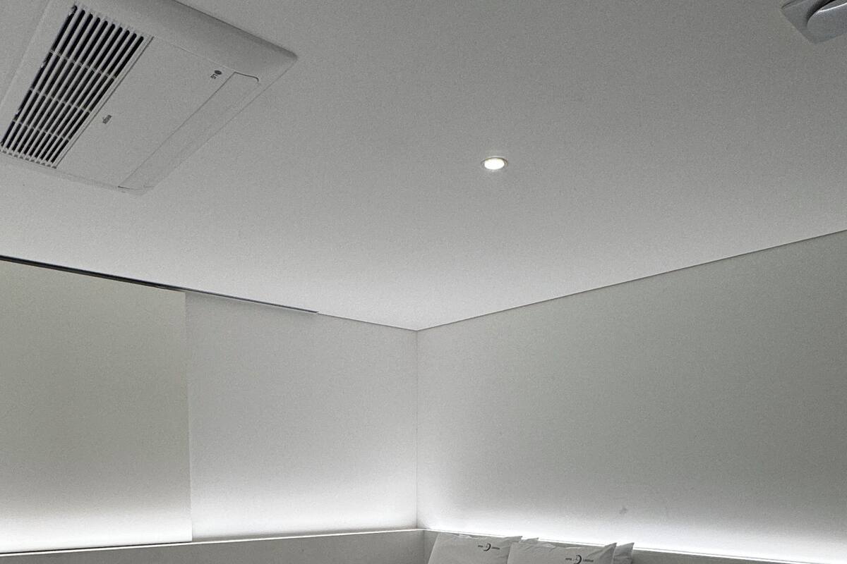 A modern, minimalistic bedroom with a bed, a white chair, and a bedside table.