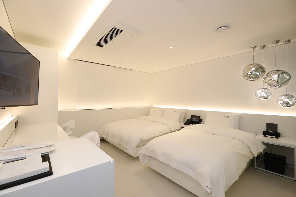 A modern hotel room with two beds, a desk, and a flat-screen TV.