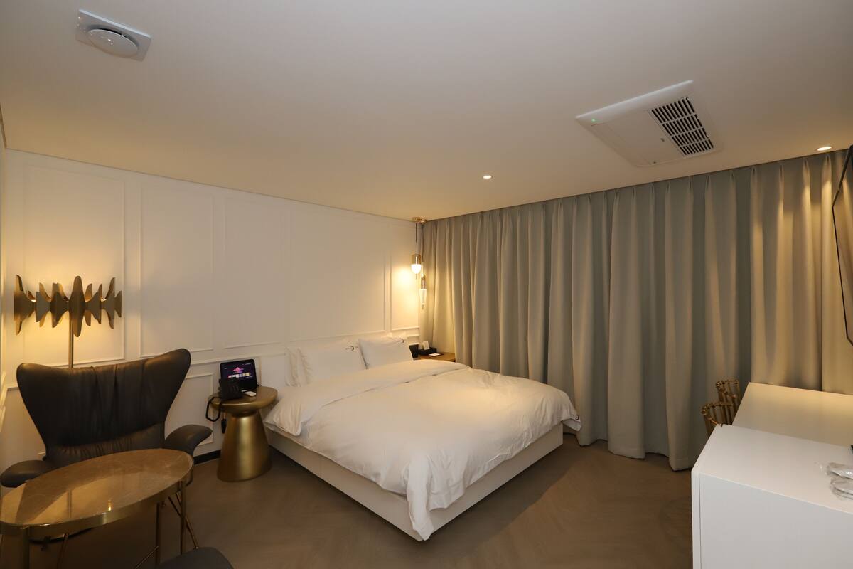 A modern hotel room with a large bed, a desk, a chair, and a small table.