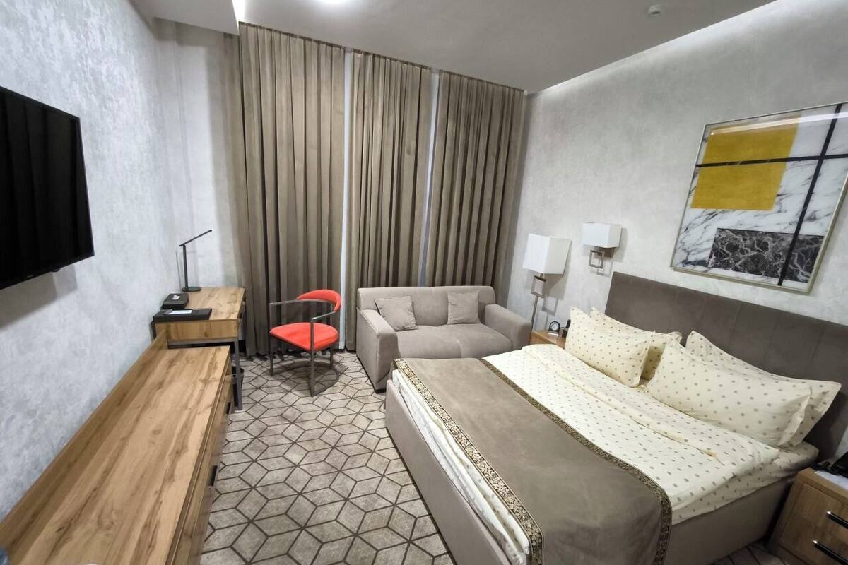 A hotel room with a bed, a desk, a chair, a sofa, and a TV.