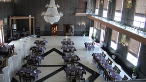 Een ruime hotellobby met diverse eetgedeeltes, een weelderige kroonluchter en een balkon met uitzicht op het interieur.