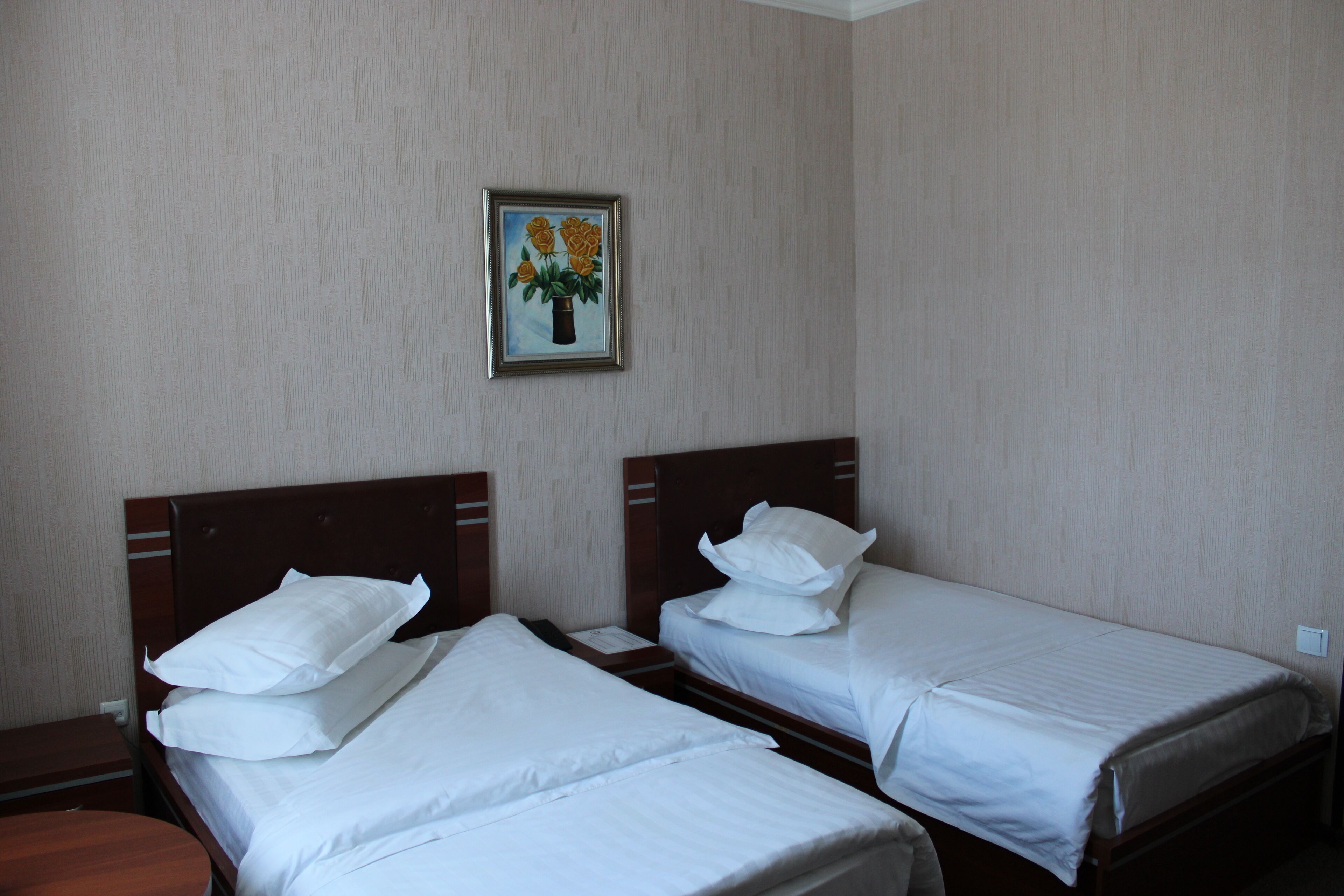 Habitación de hotel con dos camas individuales, una mesita de noche, un cabecero de madera y un cuadro en la pared.