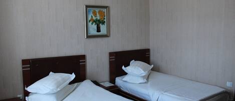 Habitación de hotel con dos camas individuales, una mesita de noche, un cabecero de madera y un cuadro en la pared.