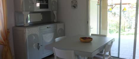Un comedor con una mesa y sillas blancas, un cuenco decorativo sobre la mesa, y una cocina con armarios y un microondas.