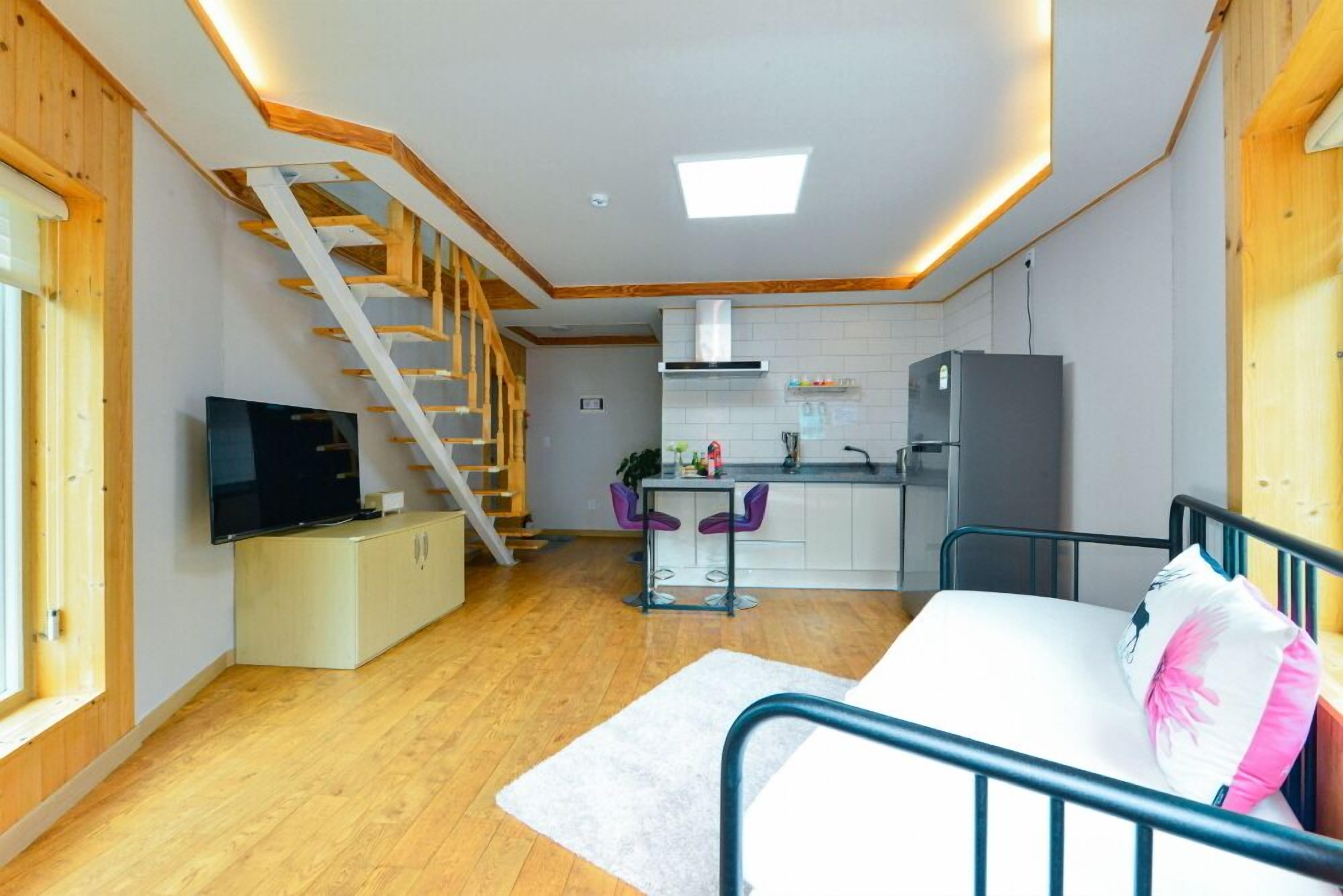 Un espacio habitable compacto con una escalera de madera, una kitchenette, un sofá y un televisor.