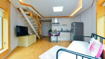 Un espacio habitable compacto con una escalera de madera, una kitchenette, un sofá y un televisor.