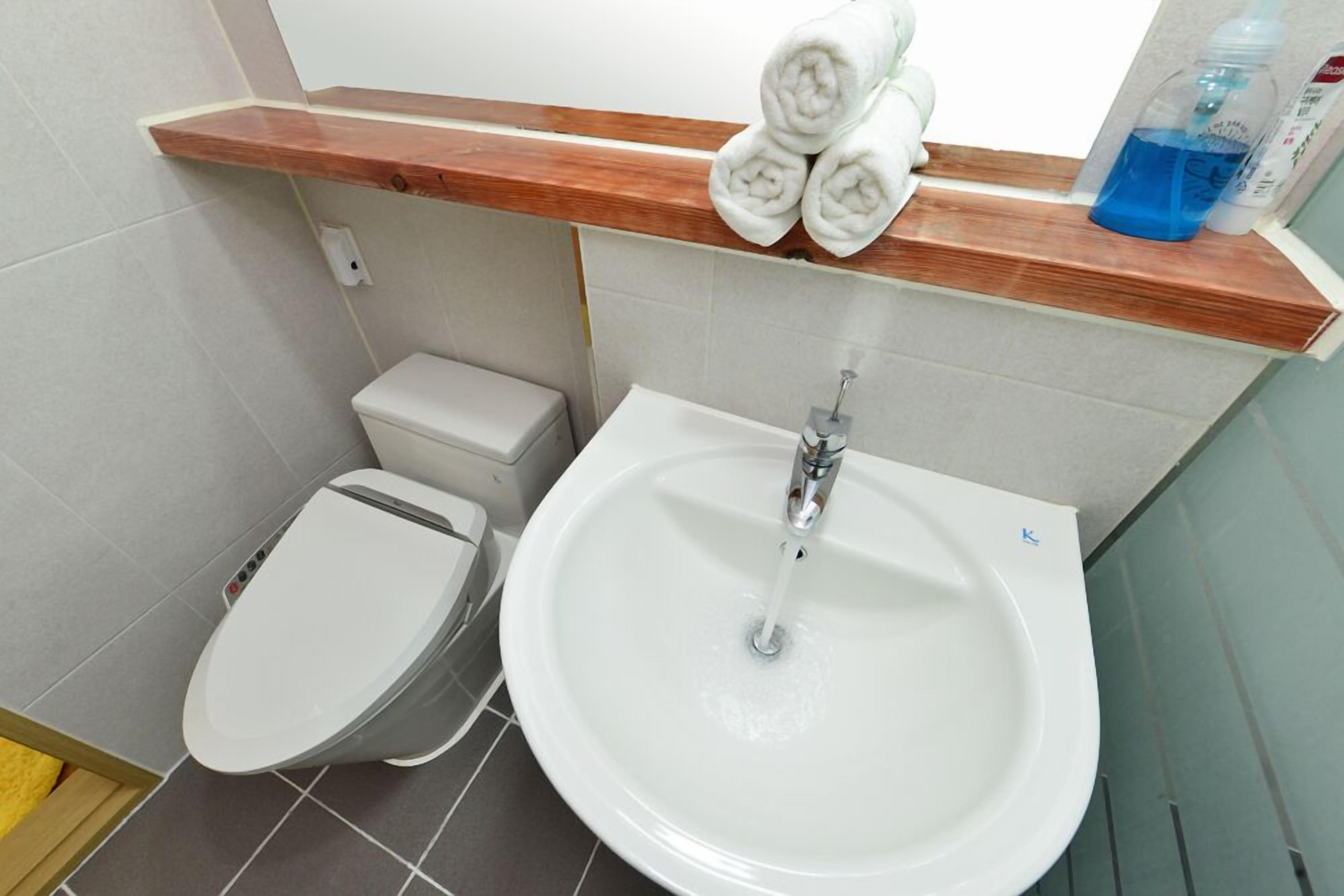 A bathroom with a toilet, sink, and a wooden shelf with towels and toiletries.