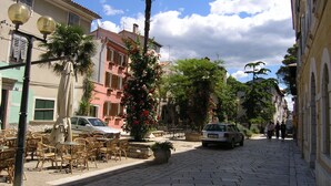 A cobblestone street lined with buildings, outdoor seating, and a parked car.