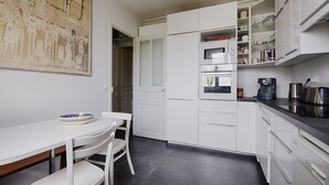 A modern kitchen with white cabinets, a dining table with chairs, and a coffee maker. - Suburban Peace in Neuilly-Sur-Seine, by Veeve (Paris)