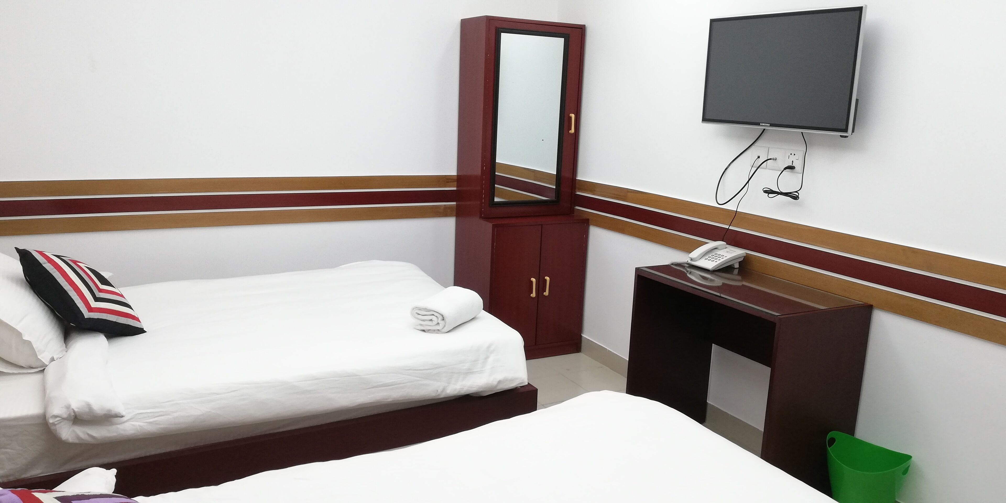 Una camera d'albergo con un letto singolo, un armadio in legno, una scrivania con telefono e una televisione fissata al muro.