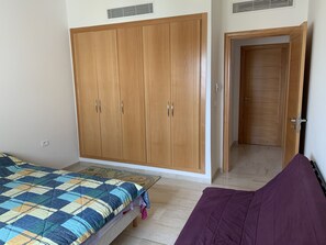 Un dormitorio con un amplio armario de madera, una cama con colcha de colores y una manta morada.
