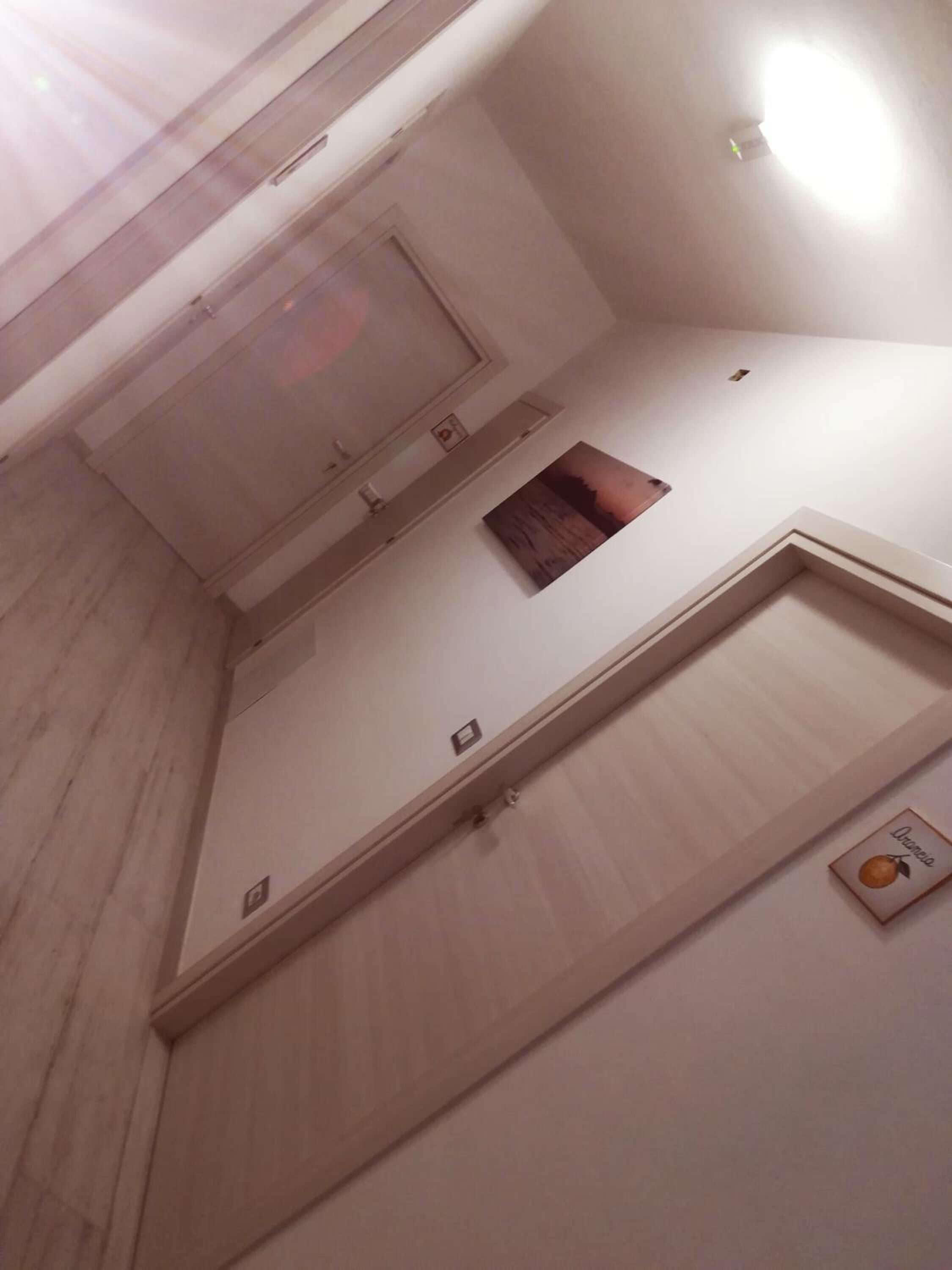 A room with a wooden floor, a ceiling light, a small window, and a door.