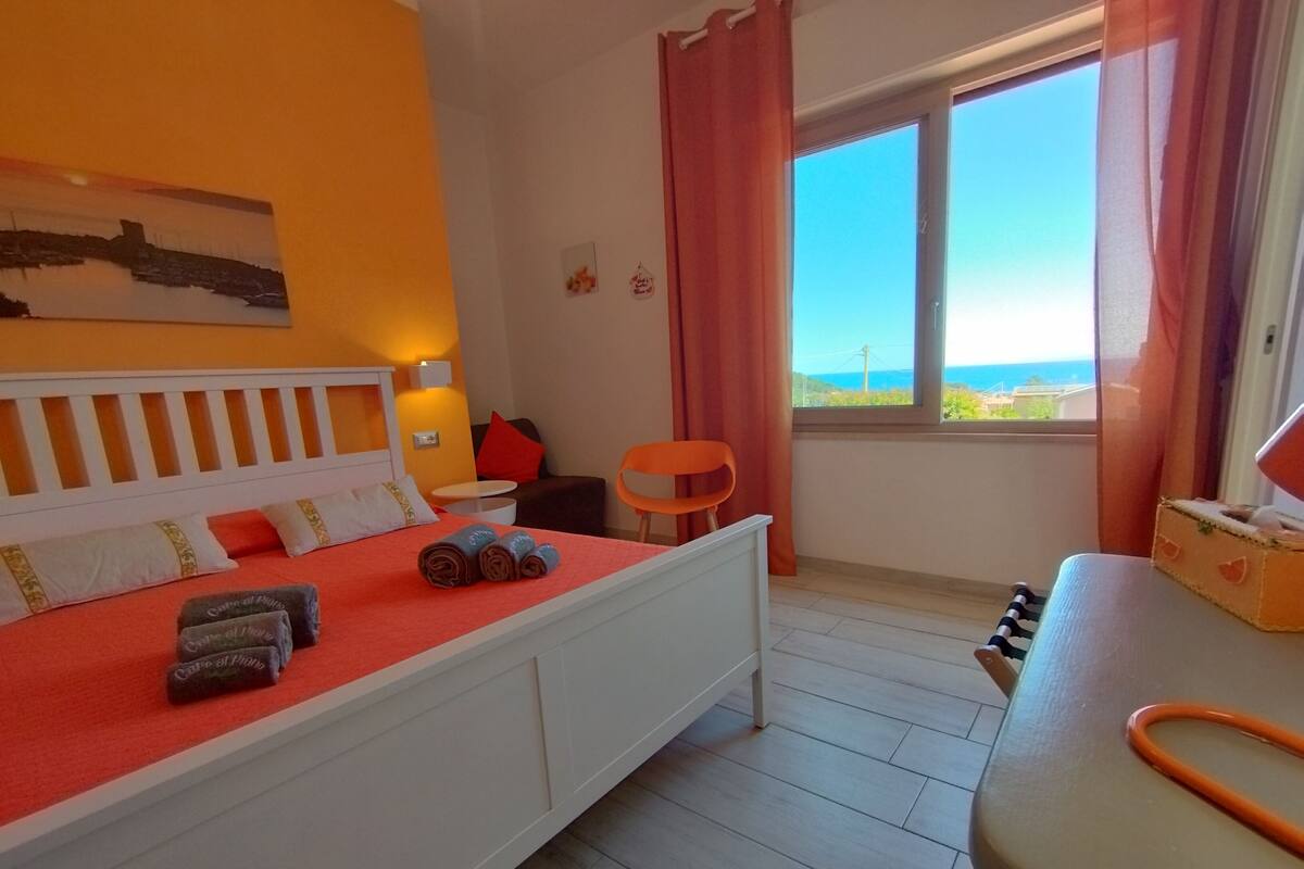 Une chambre d’hôtel avec un lit, une petite table, une chaise, une fenêtre donnant sur un beau paysage et un tableau accroché au mur.