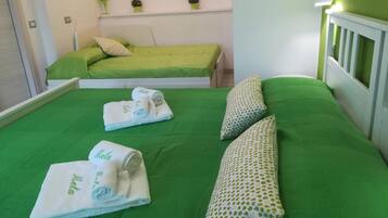 Habitación de hotel con colcha verde, dos almohadas y dos toallas enrolladas con la marca 'Mela'.