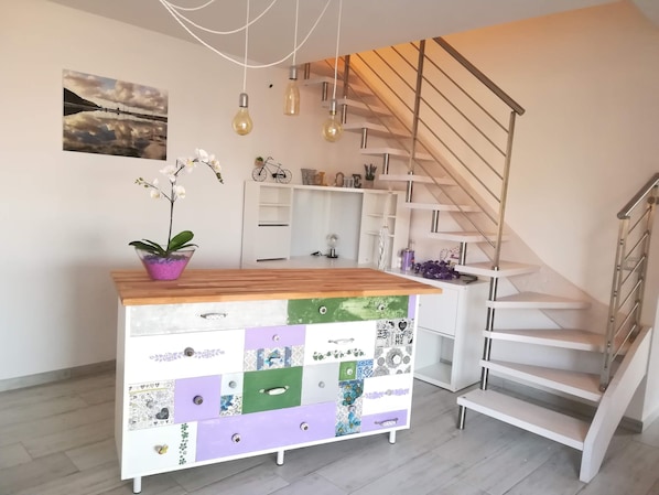 Moderni keittiö, jossa on puinen työtaso, värikäs, erilaisten kangaspalojen yhdistelmistä tehty kaappi ja metallikaiteella varustettu portaikko.