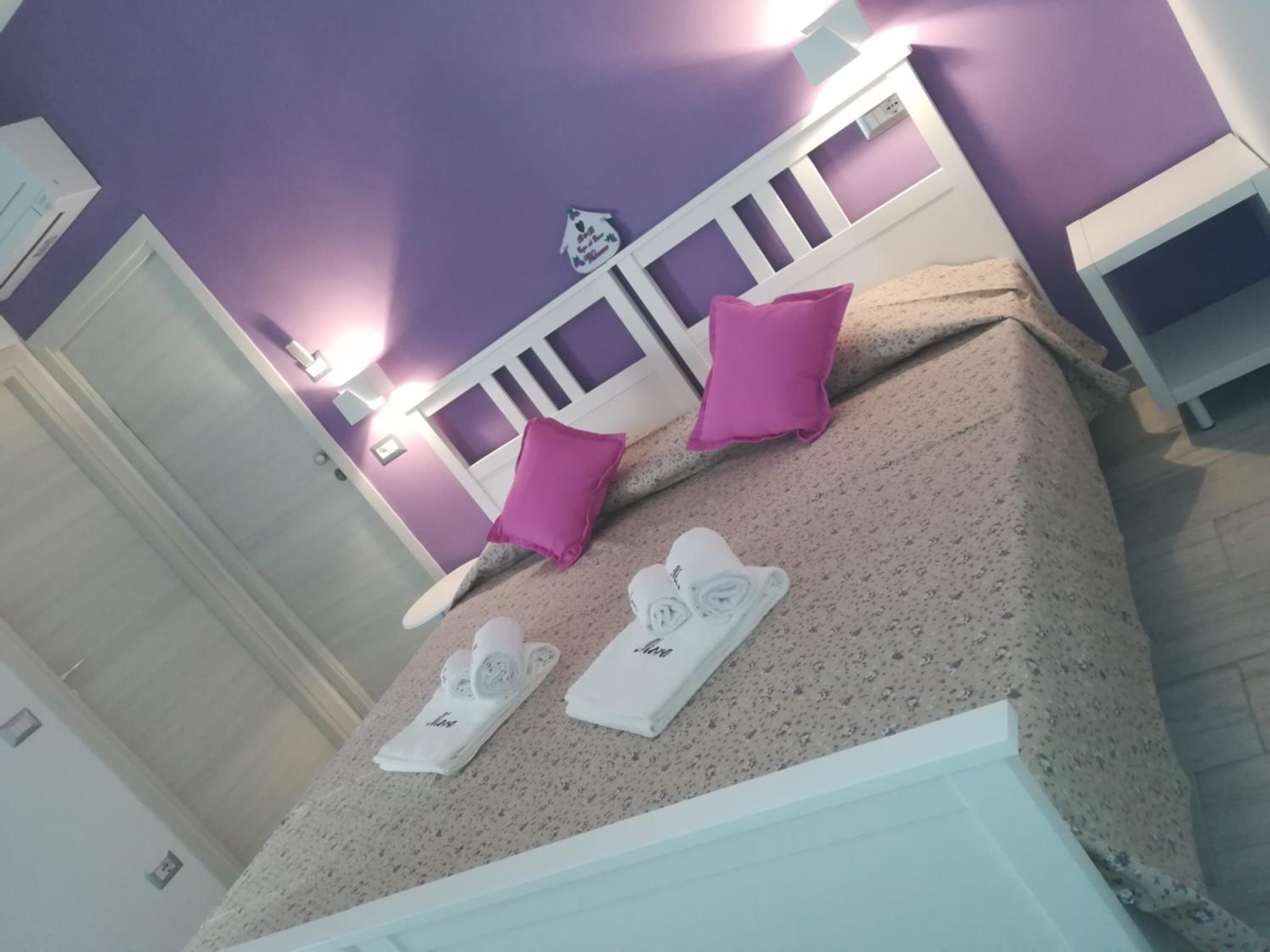 A bedroom with a bed, two pillows, a nightstand, and a wall-mounted light fixture.