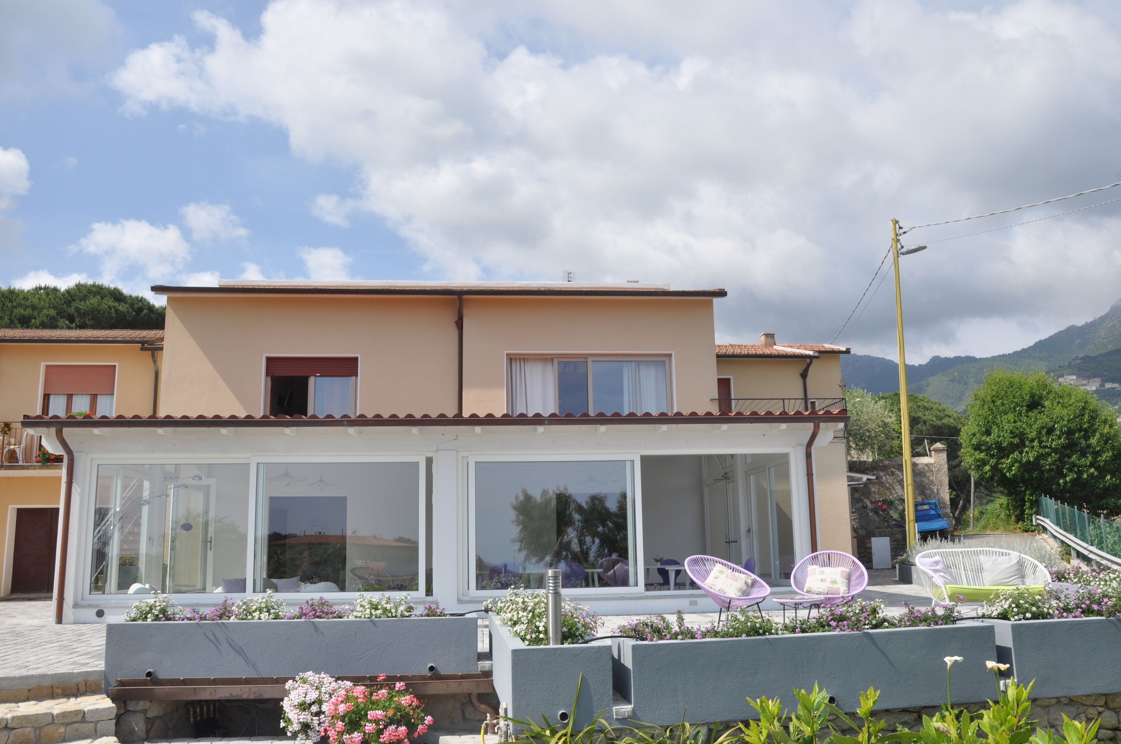 A two-story house with a balcony, large windows, and outdoor seating.