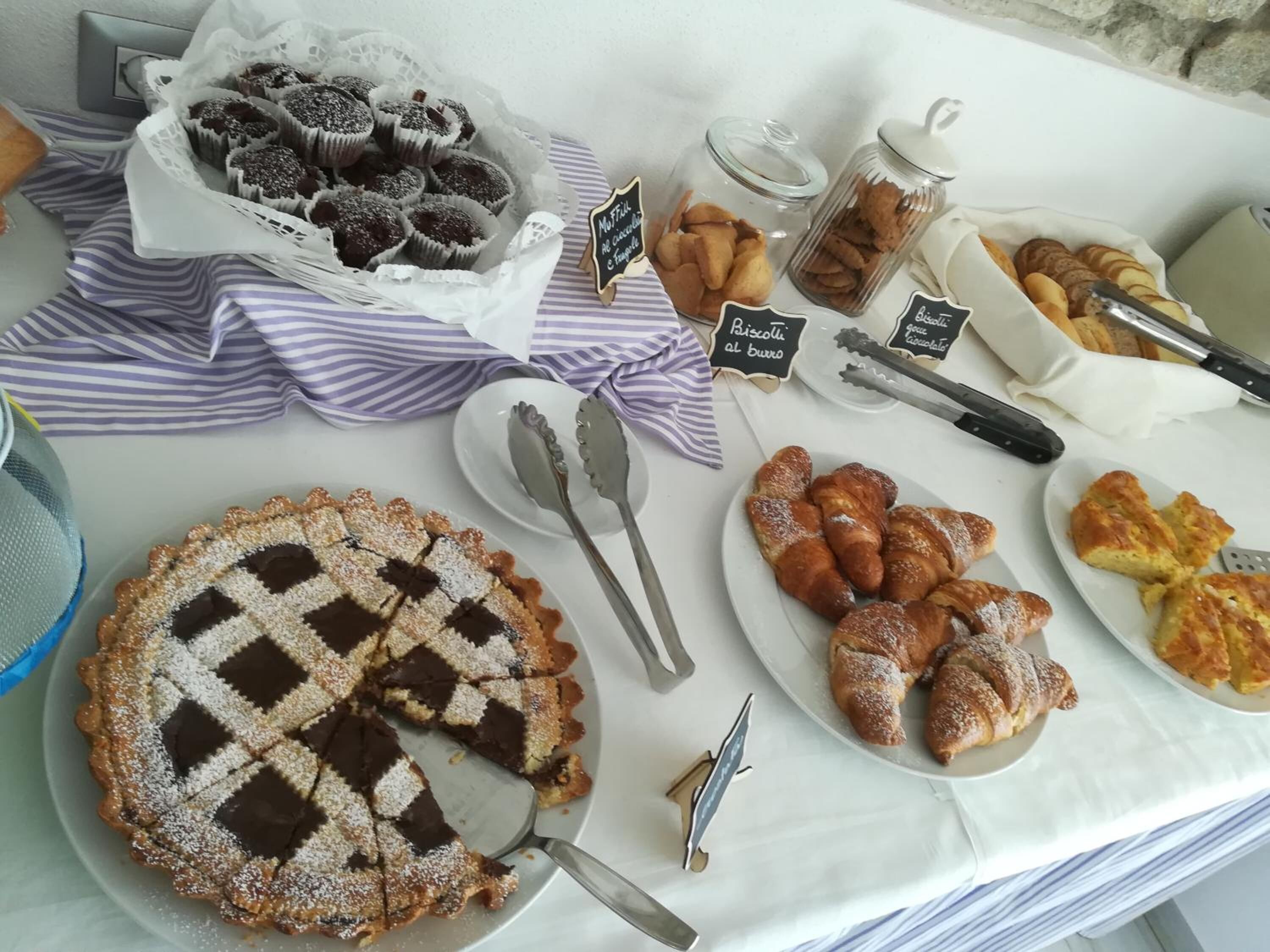 A buffet table with various baked goods including muffins, biscotti, croissants, and a chocolate tart.