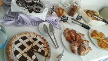 A buffet table with various baked goods including muffins, biscotti, croissants, and a chocolate tart.