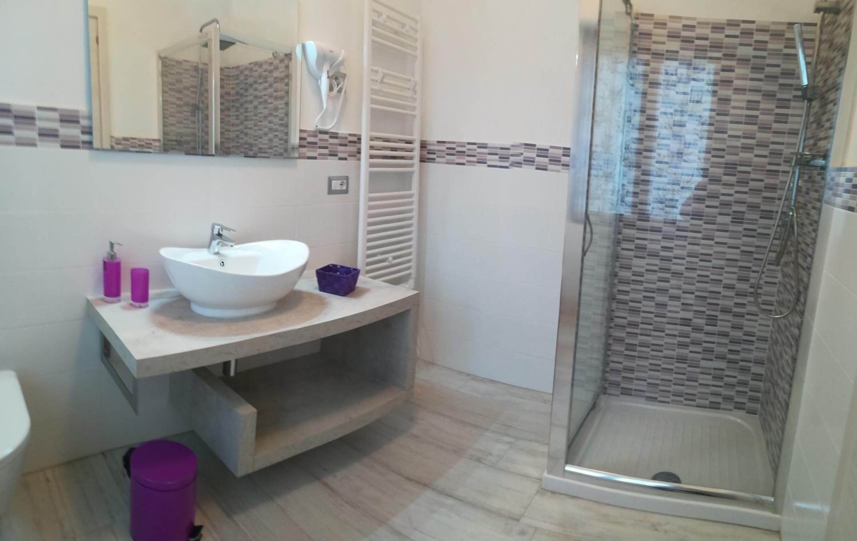Un baño con un lavabo blanco, un espejo, cabina de ducha y suelo de baldosas.