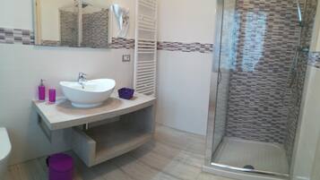 Un baño con un lavabo blanco, un espejo, cabina de ducha y suelo de baldosas.