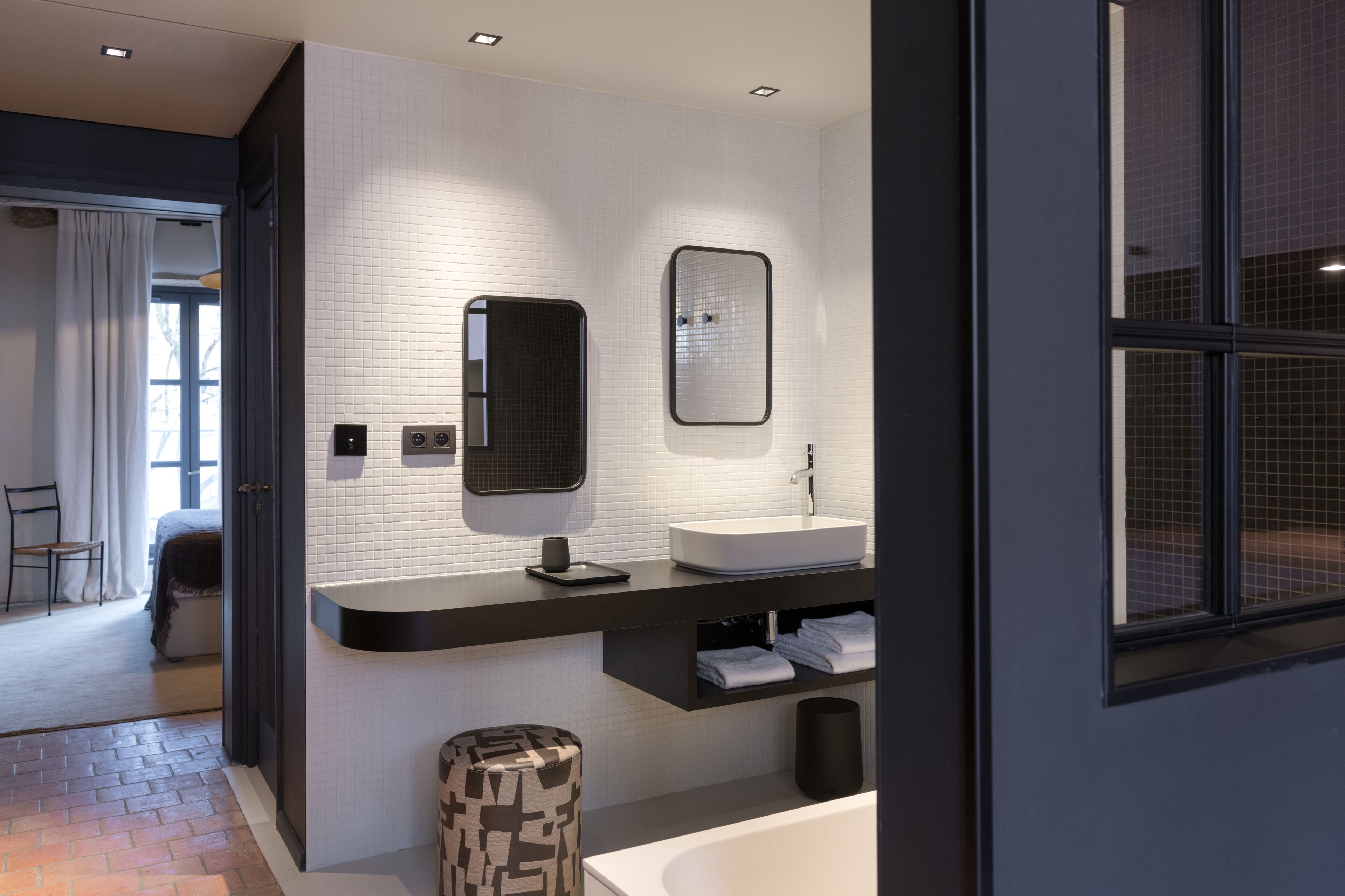 Un baño moderno con pared de azulejos blancos, encimera negra, lavabo blanco y un espejo grande.