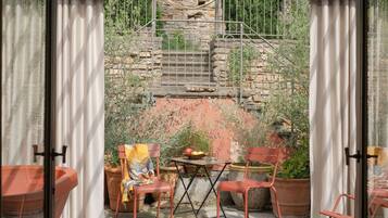 Un invernadero con puerta de cristal, una mecedora, una mesa y plantas en macetas.