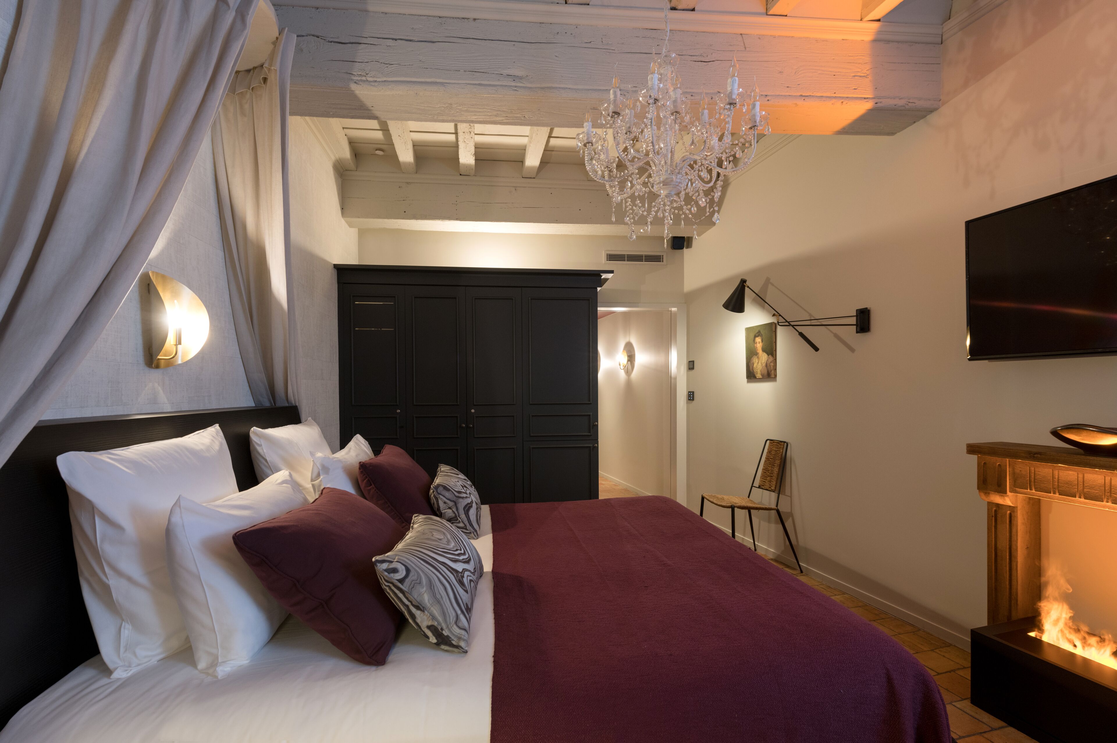 Un dormitorio con cama, candelabro, chimenea y televisor.